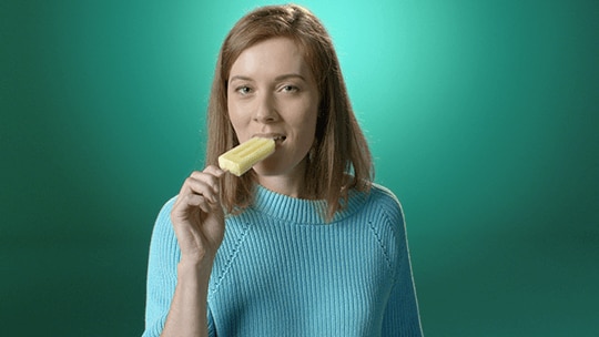 Frau ist ein gelbes Capri Eis und lächelt.